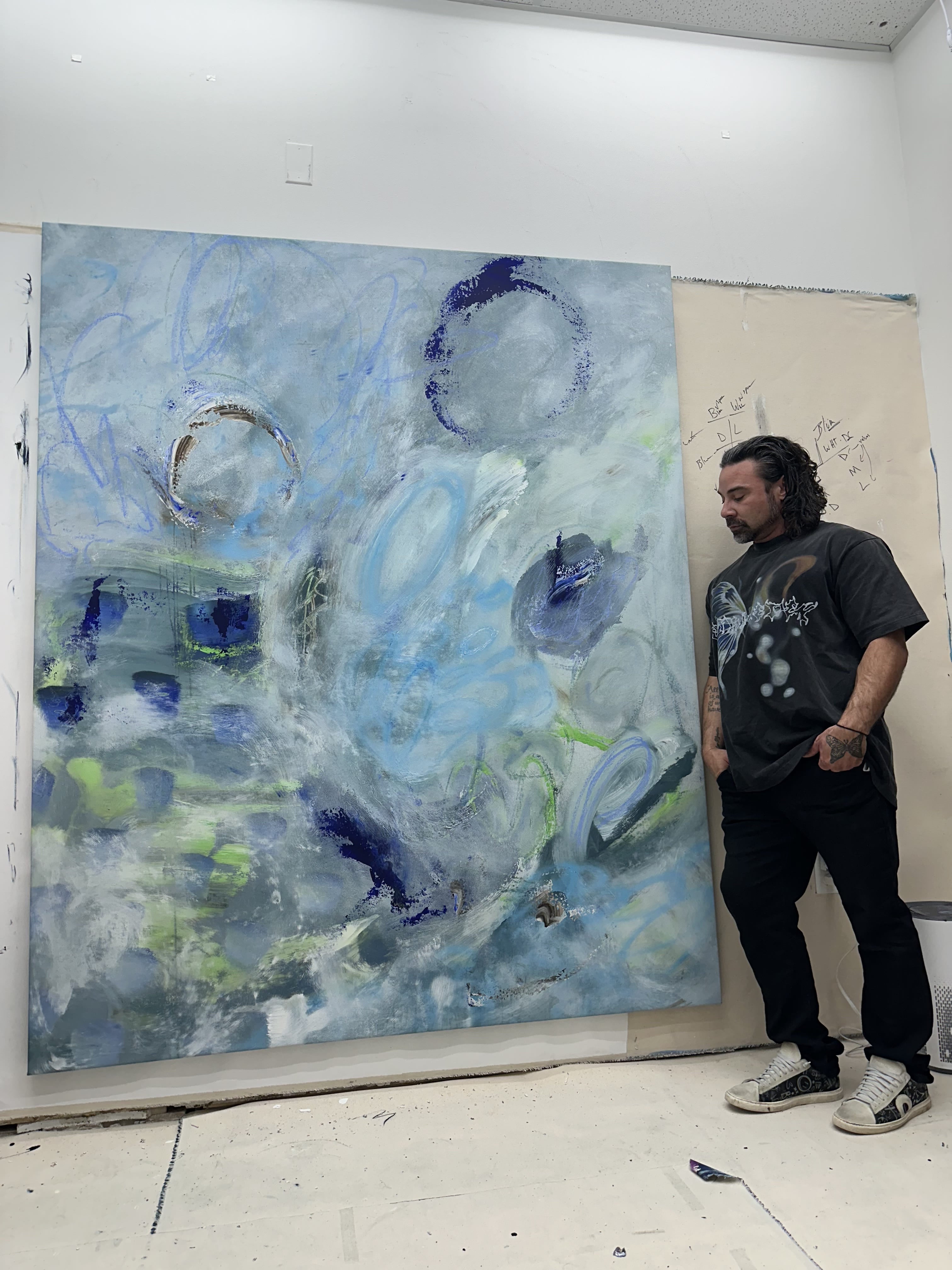 Person standing next to a large abstract painting with blue and white tones.